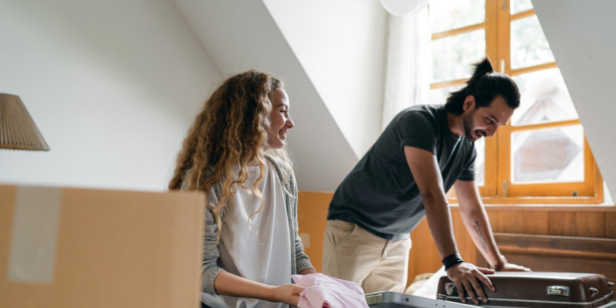 A pair of couple packing clothes and other smaller items on their luggage as they prepare to move home