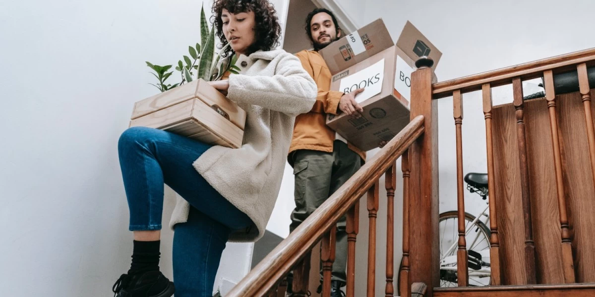 A pair of couple carrying potted plant and a box of books to move it themselves