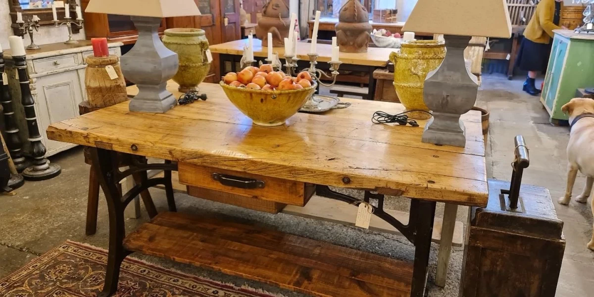 An antique wooden table, with several pieces of antique furniture in the background, displayed for sale at Country Trader in Greytown.