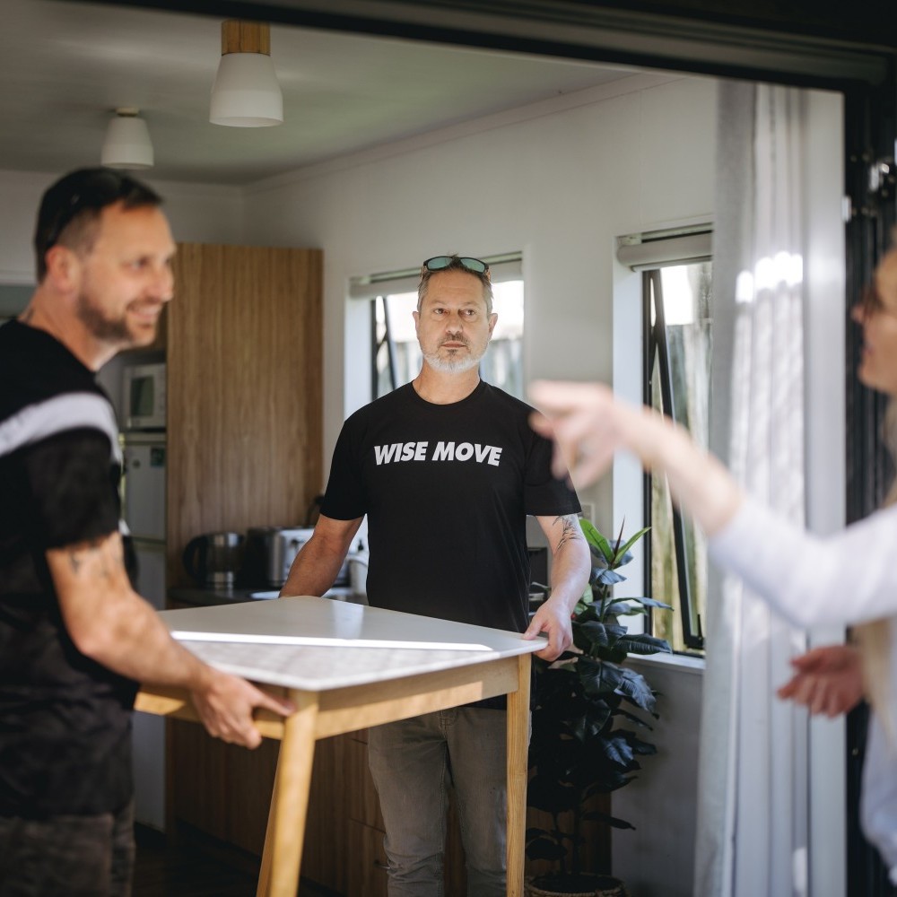 A woman giving instructions to to movers on where to put the table they are carrying