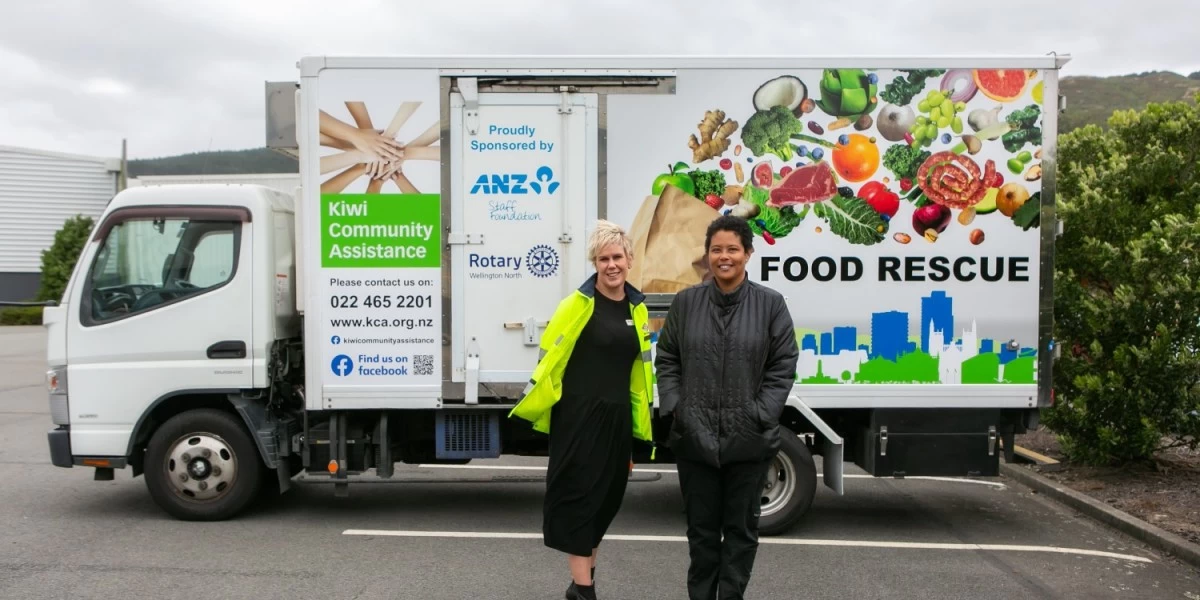 Two volunteers posing for a photo in front of Kiwi Community Assistance Truck