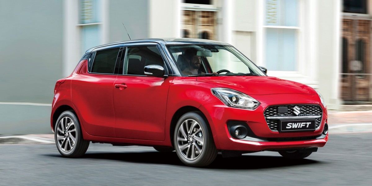 A man driving a red Suzuki Swift, a compact car which is one of the most popular cars in New Zealand, due to its reliability and affordability
