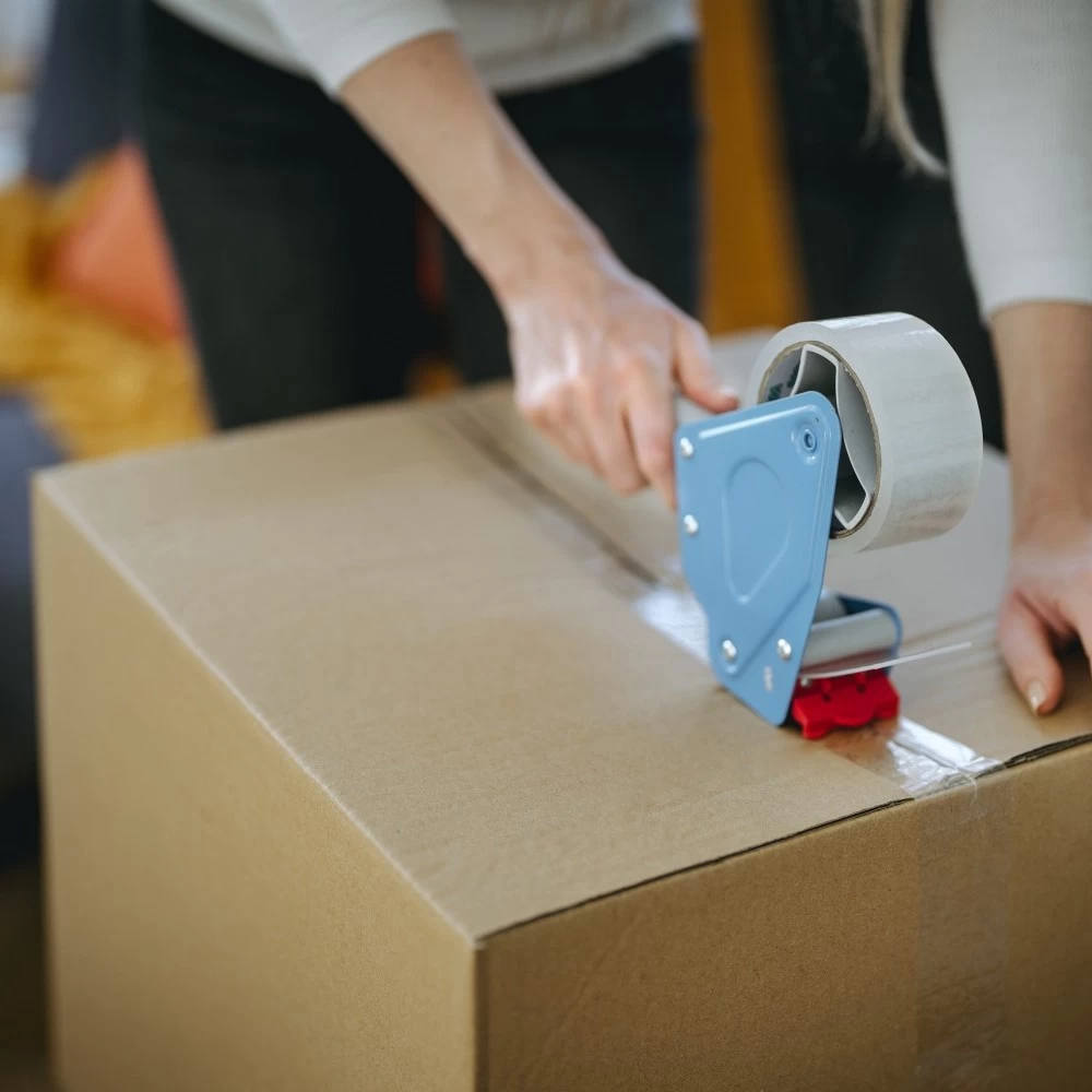 A woman closing a moving box securely with a packaging tape