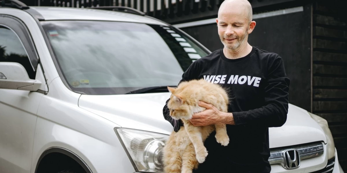 A pet mover carrying a cat while standing in front of a vehicle