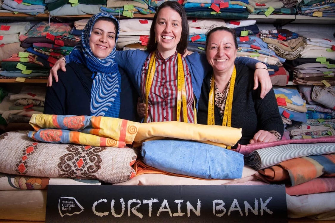 Volunteers at Wellington Curtain Bank smiling for a photo in front of folded fabrics 