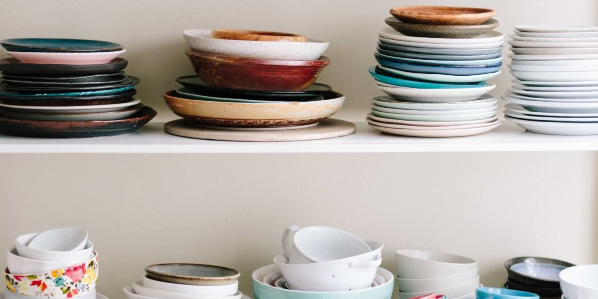 Mismatched and rarely used dinnerware piled on top of each other in a kitchen cupboard