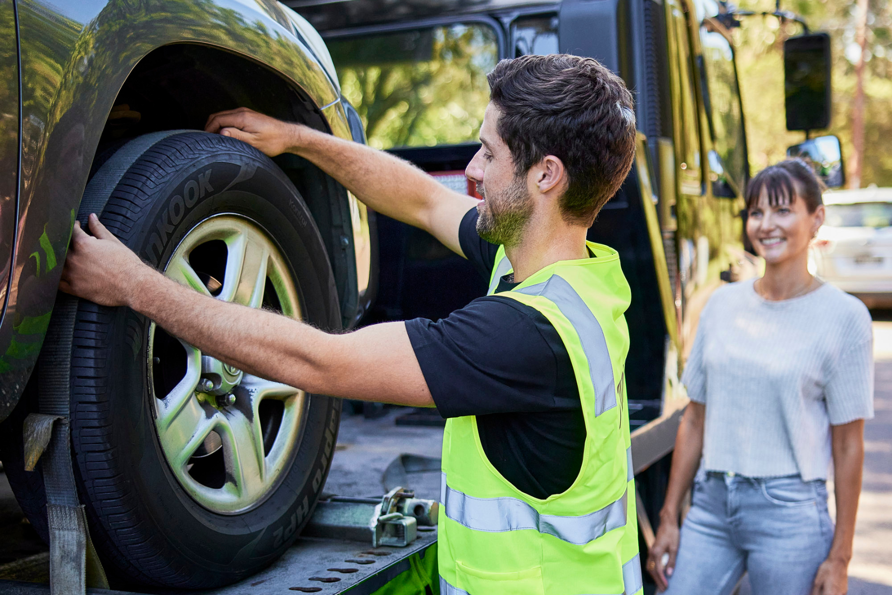 car transporter strapping in tires of car on the back of a trailer with car owner watching