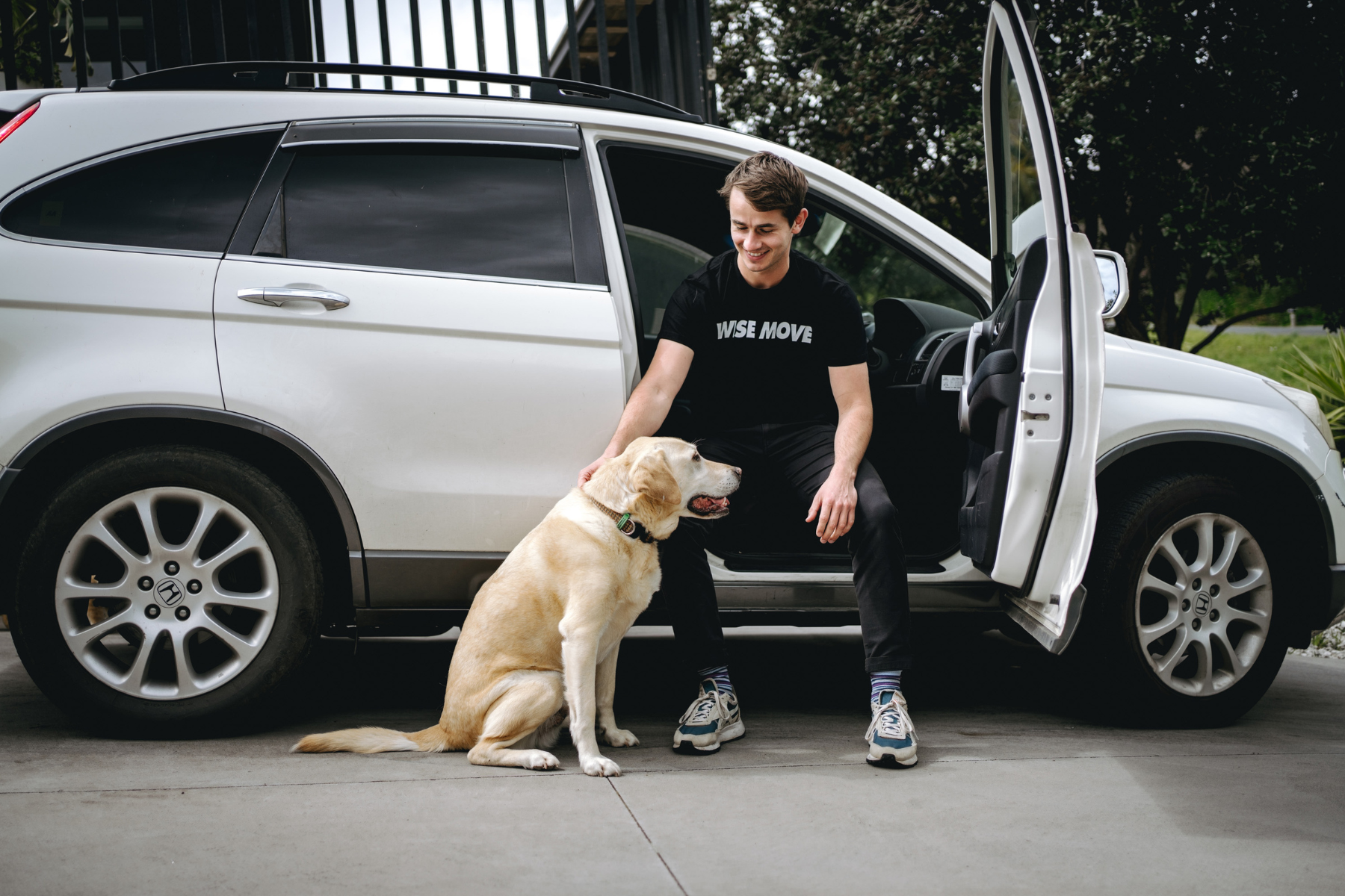 Student petting dog sitting inside car about to transport it to university